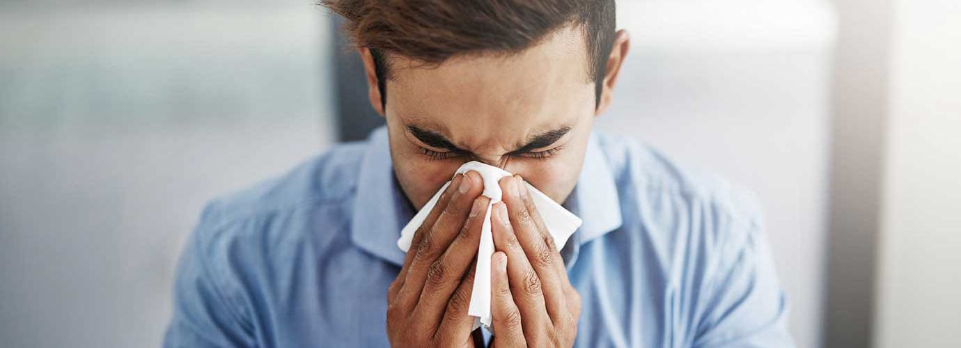 Young man sneezing and blowing his nose with a tissue