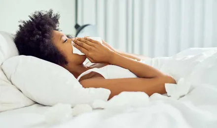 Young woman in bed blowing her nose