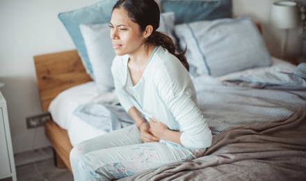 Woman sitting on her bed with abdominal pain