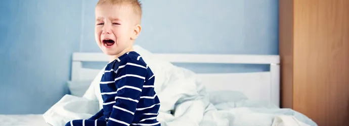 A young child sat on an unmade bed crying
