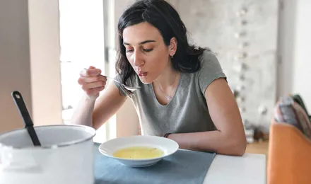 Woman with dark hair eating broth at home as a remedy for watery eyes with a cold
