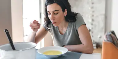 Woman with dark hair eating broth at home as a remedy for watery eyes with a cold